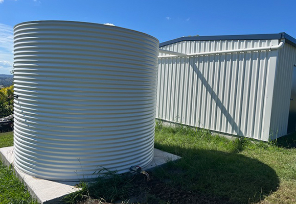 Round rainwater tank on a concrete base beside a shed